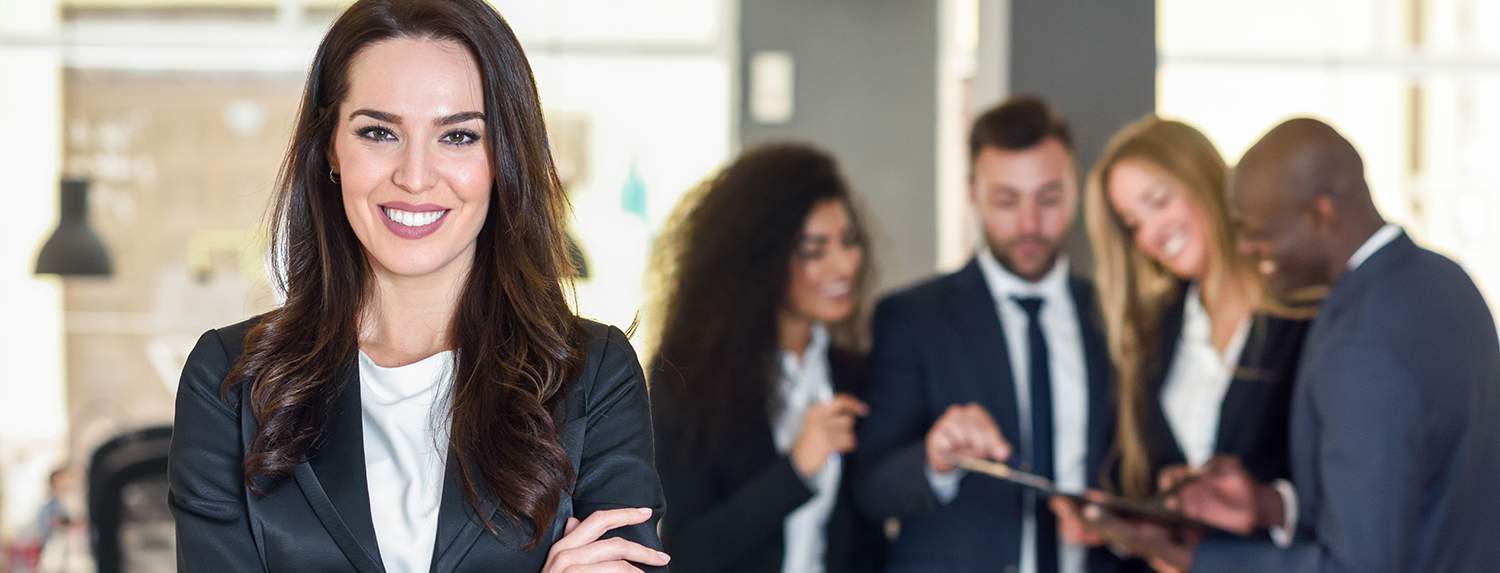 Businesswoman leader looking at camera in modern office with multi-ethnic businesspeople working at the background. Teamwork concept. Caucasian woman.